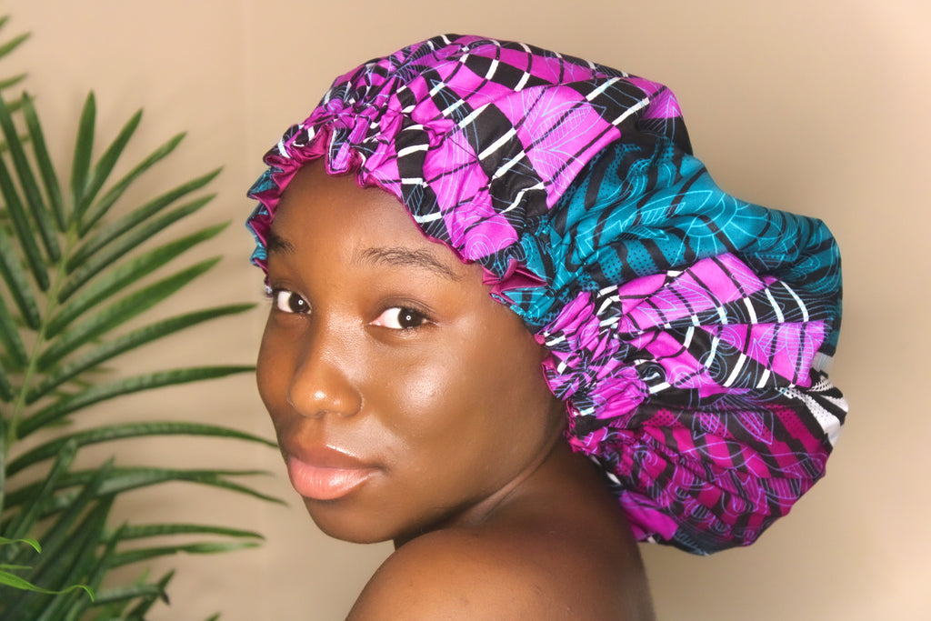 Brown skin model wearing a large satin lined bonnet in multicolor like blue, pink, white, black. This bonnet is a kente bonnet, african print satin lined, ankara bonnet, hair bonnet. Lined with black Satin