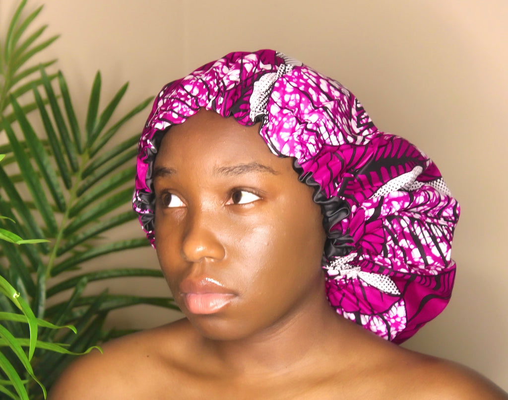 Brown skin model wearing a large satin lined bonnet in multicolor like pink, white, black. This bonnet is a kente bonnet, african print satin lined, ankara bonnet, hair bonnet. Lined with black Satin