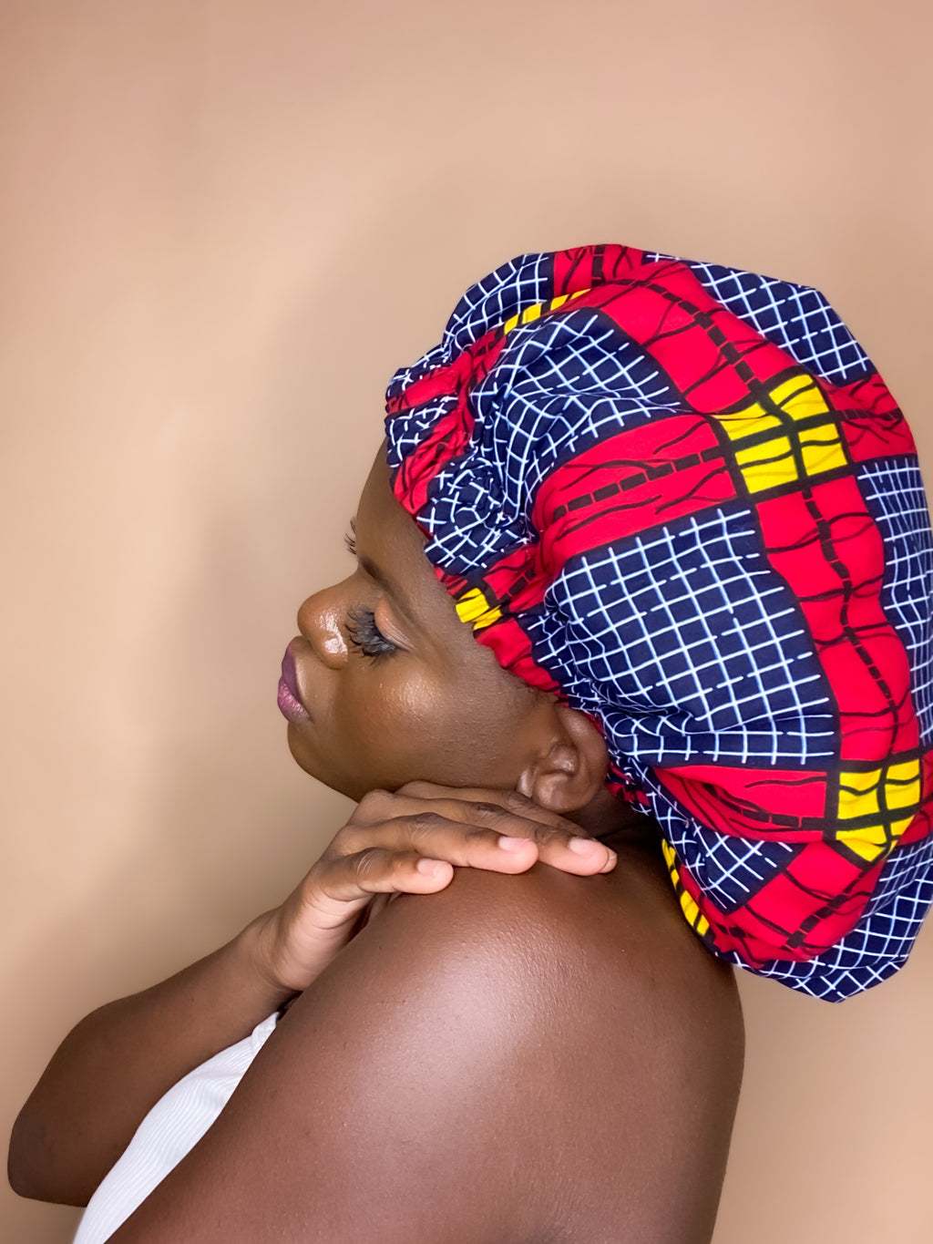 Brown skin model wearing a large satin lined bonnet in multicolor like yellow, pink, white, black, blue, red and yellow. This bonnet is a kente bonnet, african print satin lined, ankara bonnet, hair bonnet. Lined with red/blue Satin