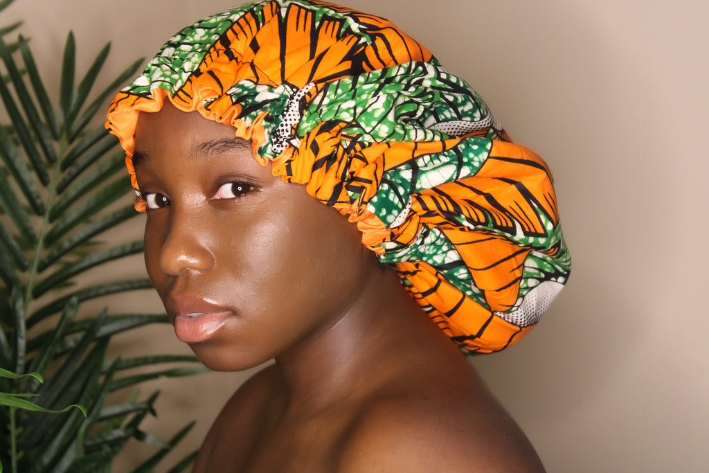 Brown skin model wearing a large satin lined bonnet in multicolor like yellow, pink, white, black, green and blue. This bonnet is a kente bonnet, african print satin lined, ankara bonnet, hair bonnet. Lined with Pink Satin