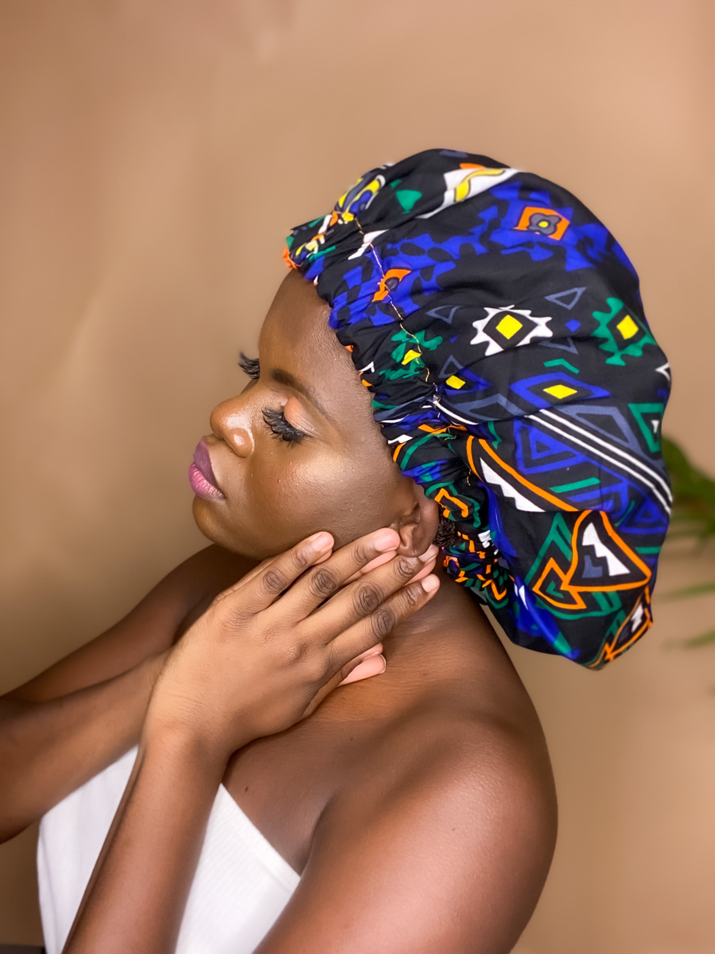 Brown skin model wearing a large satin lined bonnet in multicolor like blue, orange, white, black. This bonnet is a kente bonnet, african print satin lined, ankara bonnet, hair bonnet. Lined with blue Satin