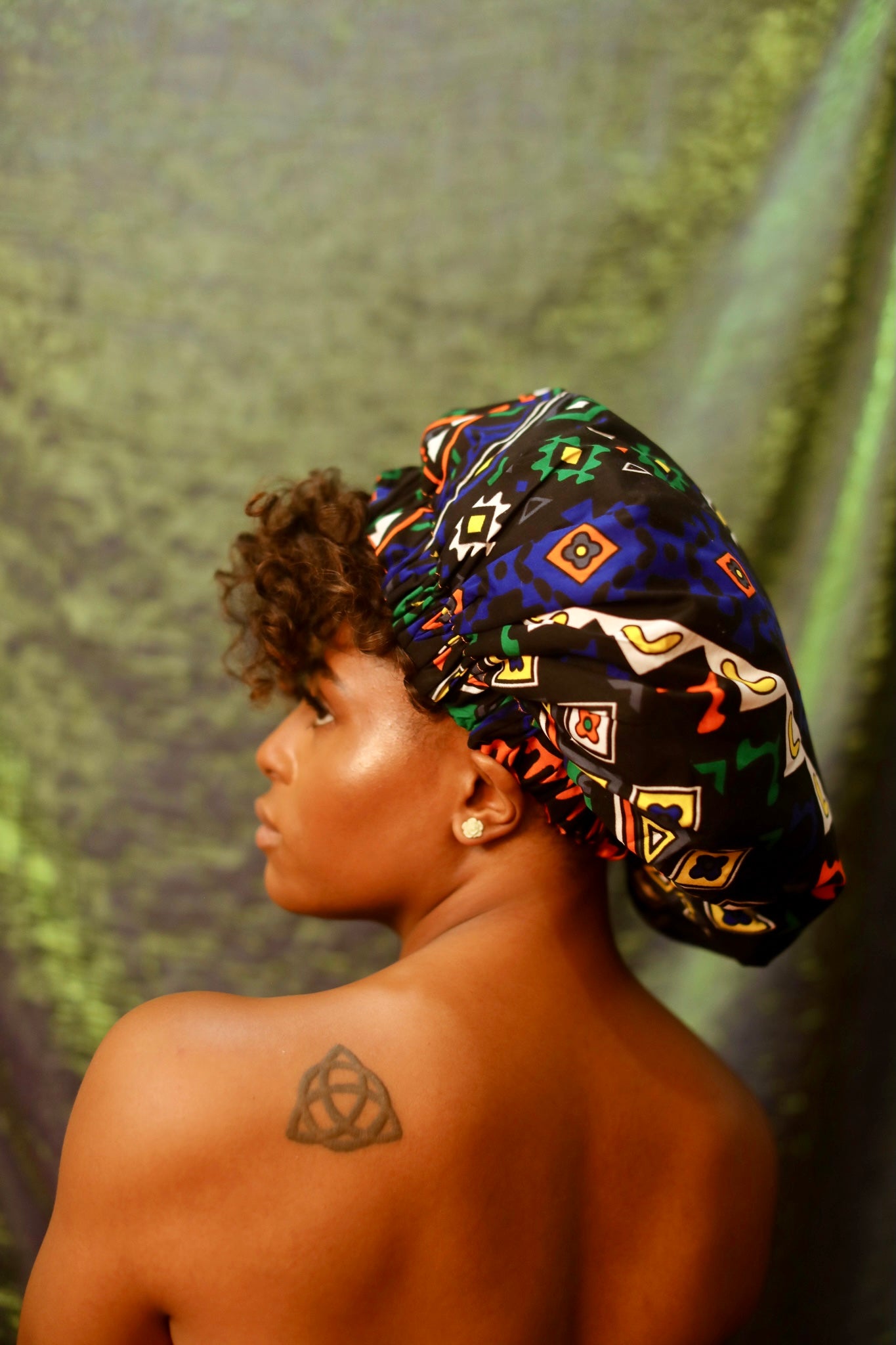 Brown skin model wearing a large satin lined bonnet in multicolor like blue, orange, white, black. This bonnet is a kente bonnet, african print satin lined, ankara bonnet, hair bonnet. Lined with blue Satin